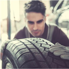 Young male mechanic looks over a car tyre in a workshop