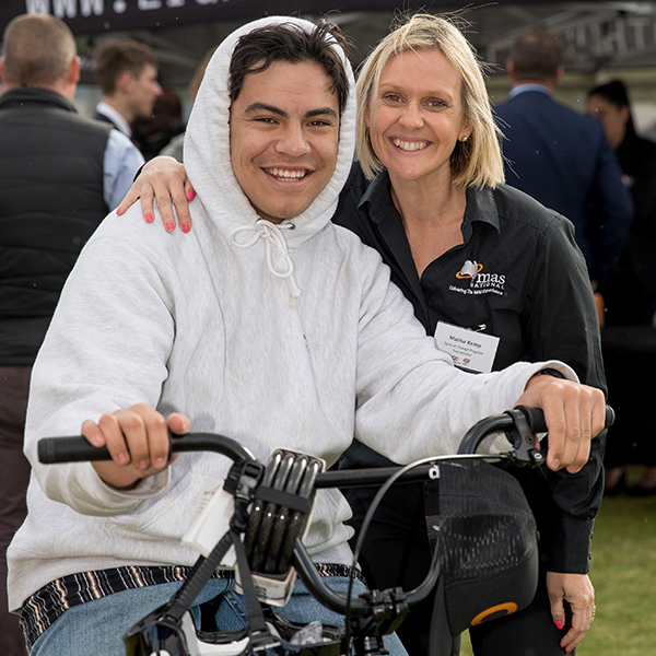 Young male sitting on a BMX bicycle stands with a female support worker, smiling at the camera
